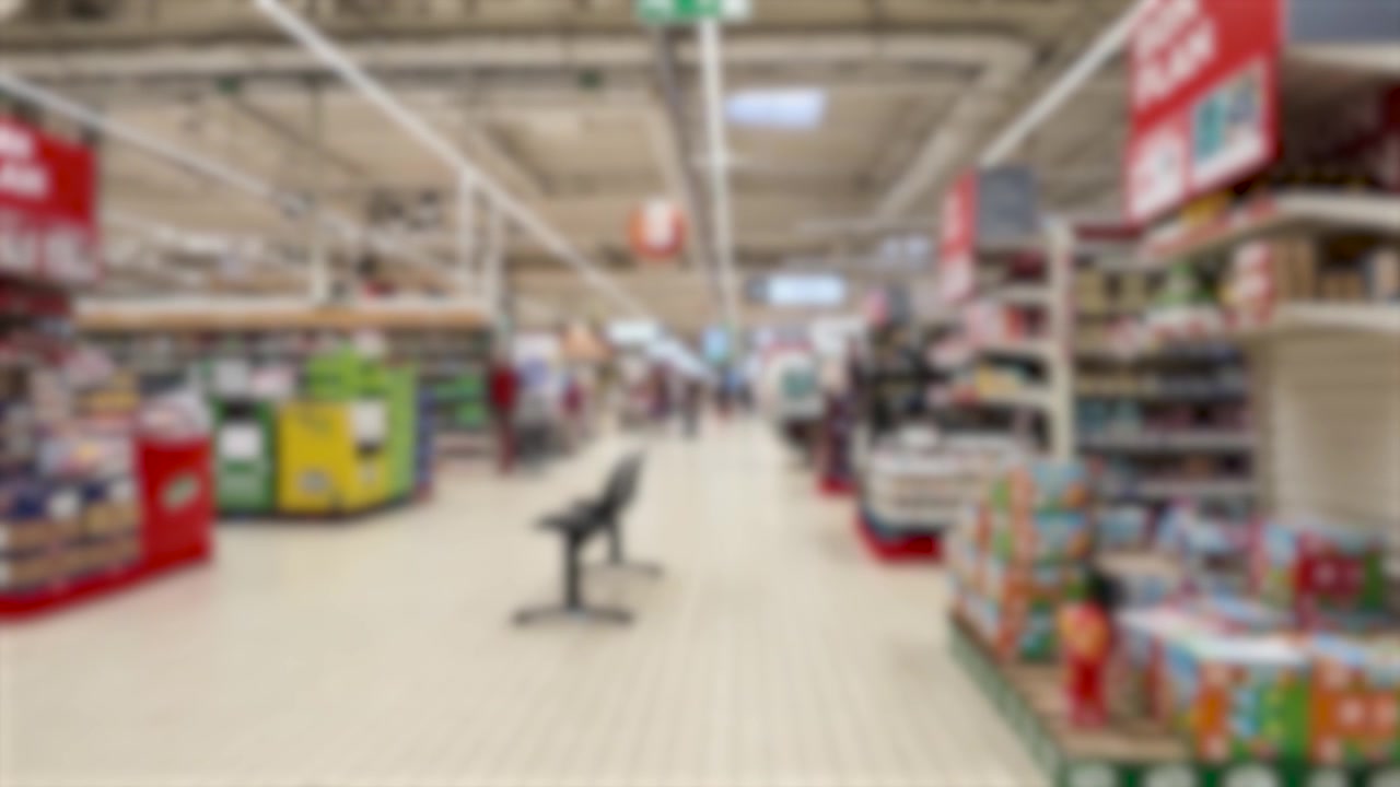 Et kamera med blød fokus bevæger sig gennem en lys fransk hypermarkedsgang forbi forskellige udstillinger med dagligvarer.