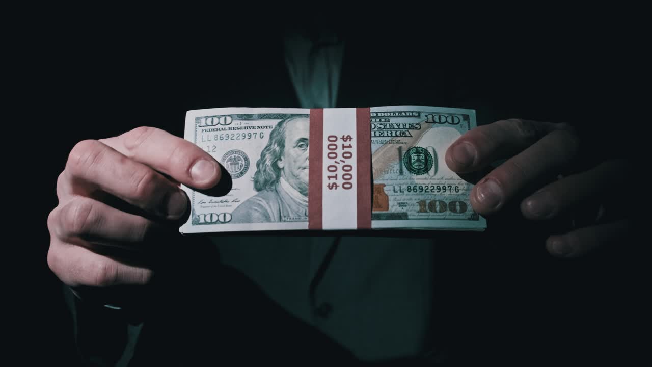 슈트를 입은 사업가는 검은 바탕에 1만 달러를 쌓아 놓은 모습을 보여준다.