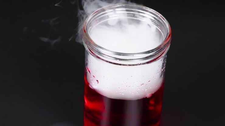 Una sequenza che mostra il ghiaccio secco che reagisce in un liquido rosso, creando nebbia e bolle in un becher di vetro.