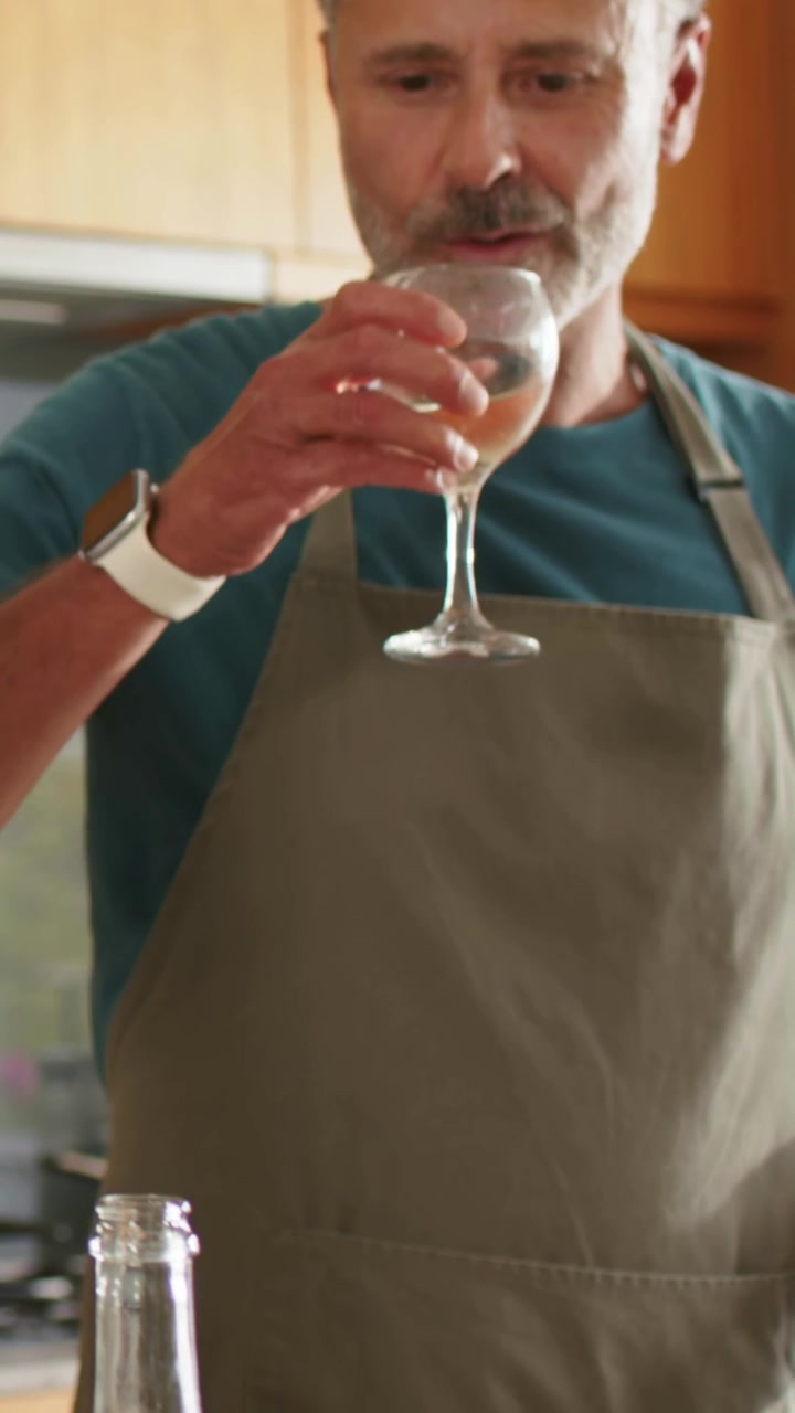 Video verticale: Si vede un bicchiere di vino e una bottiglia aperta, un cuoco con grembiule che solleva e assaggia in cucina