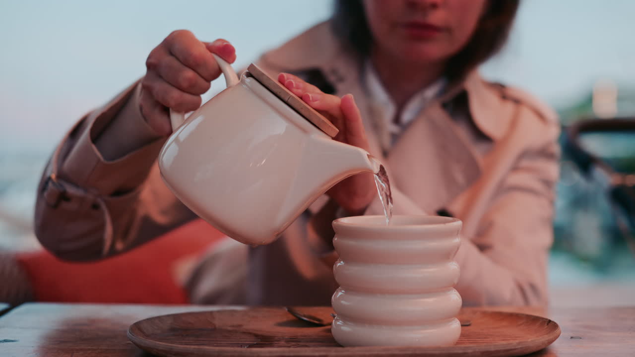 A woman pouring tea into a ceramic cup, filmed in warm evening tones