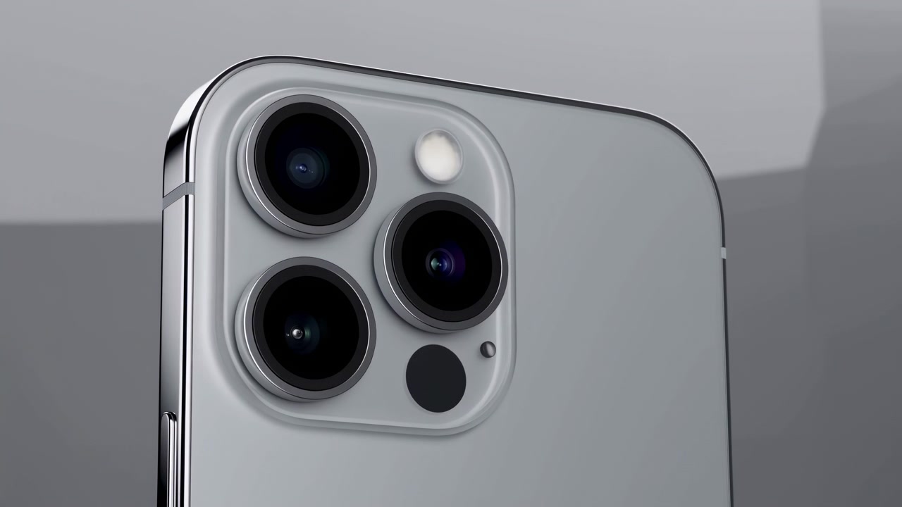Close up view of a silver smartphone corner showing three rear camera lenses and a flash, isolated against a soft gray background with even studio lighting