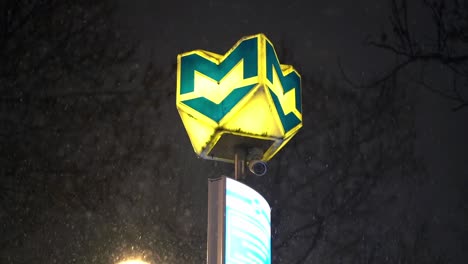 metro sign post and security camera at night as snowfalls around peacefully