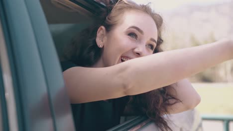 girl-with-loose-hair-laughs-in-car-against-blurred-field