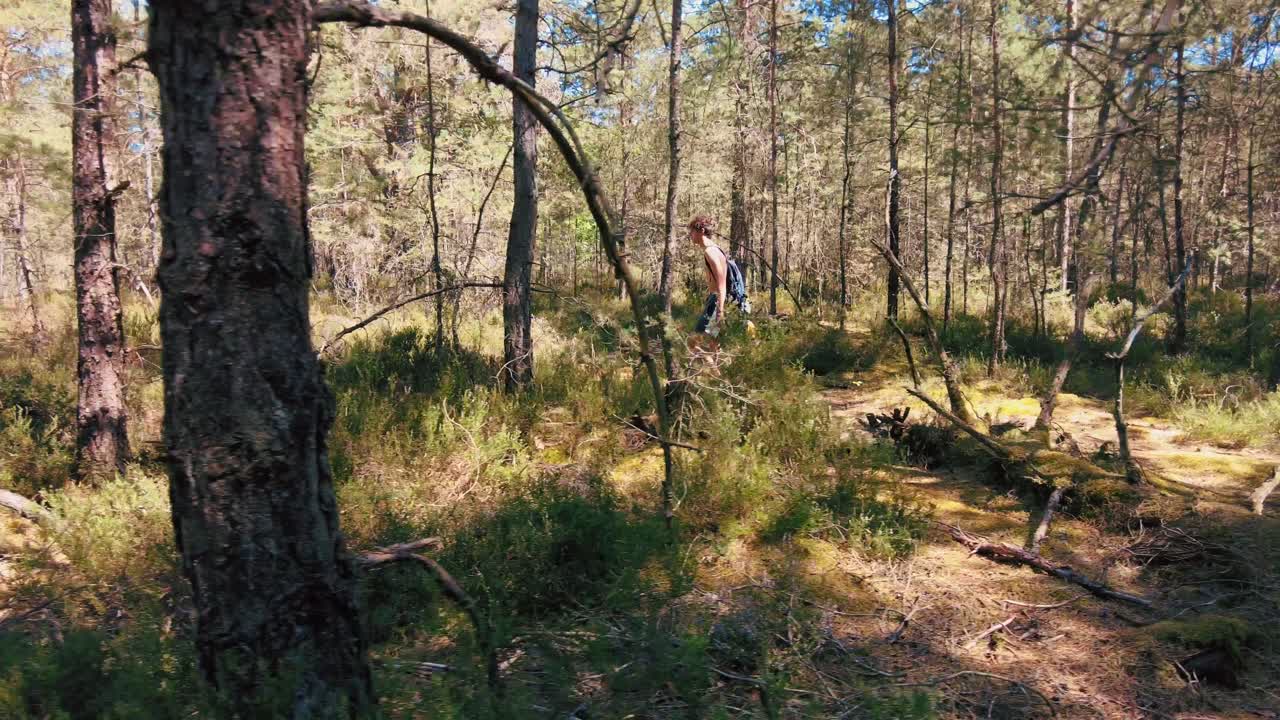 wide shot of shirtless teenage boy backpacking through forest in Fontainebleau