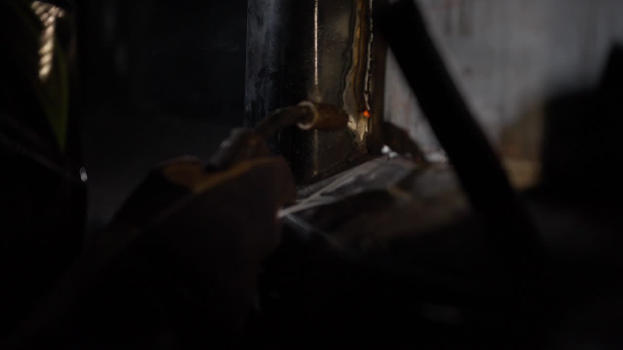A metal worker uses a torch to weld the side of a construction vehicle in a repair bay in slow motion as sparks fly