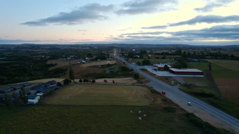 Luftaufnahme-Einer-Wiese-Mit-Einer-Einsamen-Straße-In-Chiloé-Mit-Einem-Orangefarbenen-Und-Bläulichen-Hintergrund-Mit-Wolken,-Chile