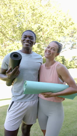vertical video: holding yoga mats, smiling couple enjoying outdoor exercise together in park