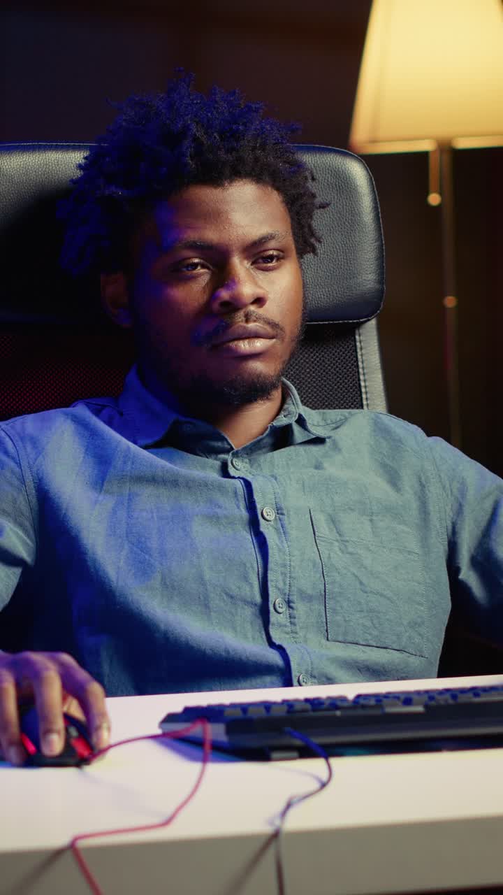 Vertical video Man playing videogames on gaming PC late at night, struggling to stay awake at desk