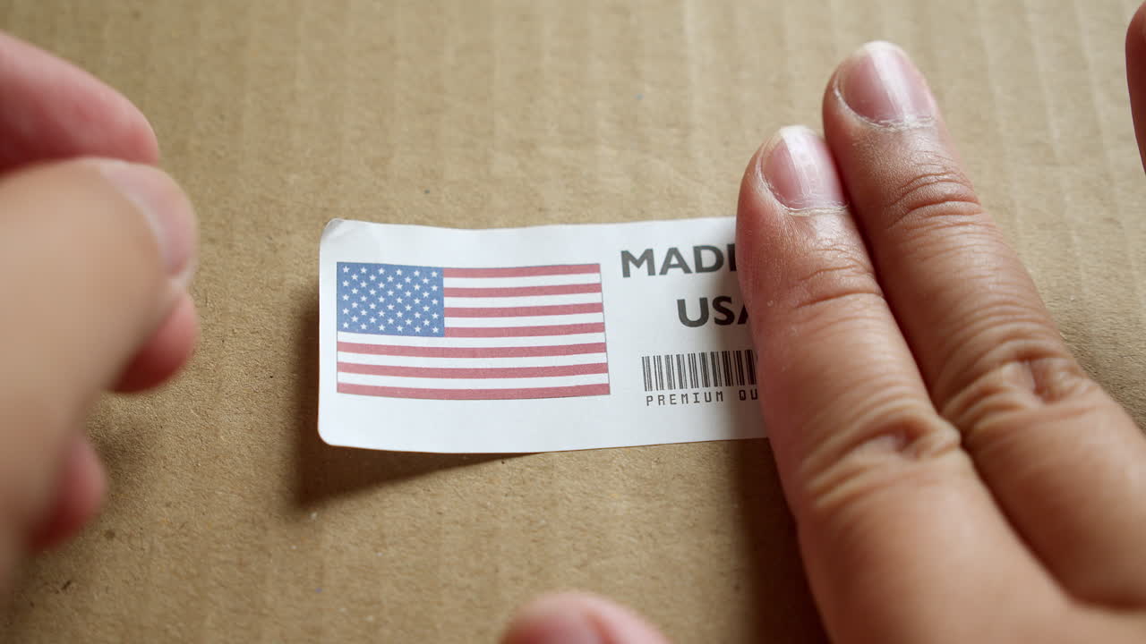 Hands applying MADE IN USA flag label on a shipping box with product premium quality barcode