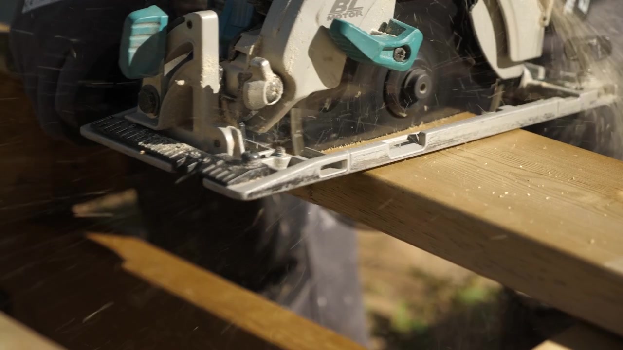 Static shot, of a carpenter, using a circular saw, to cut a deck board