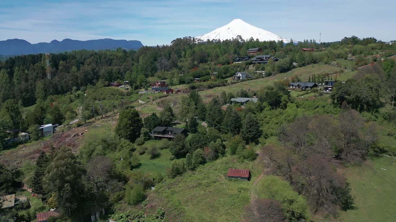 Drone Shot above Hillside Cabins and Villas Amid Lush Green Forests with the Snow-Capped Villarrica Volcano in the Background in Chile