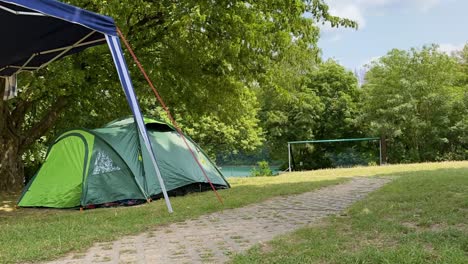 Timelapse-of-a-campsite-in-Germany-with-a-tent-and-pavilion-in-the-foreground,-large-fields-and-trees-in-the-wind