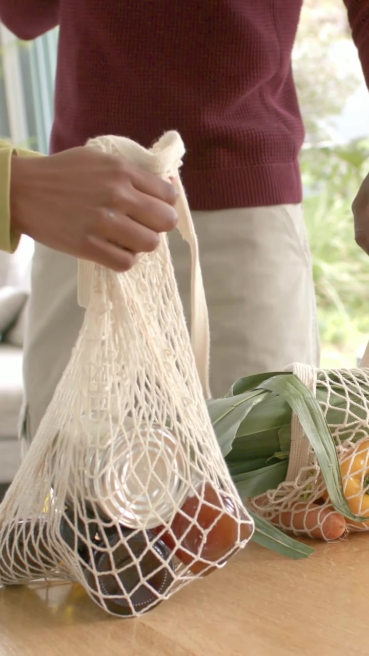 Video verticale: Entrando in casa, una donna con un top verde tiene una borsa a rete e posa il cibo sul tavolo, con spazio per il testo.