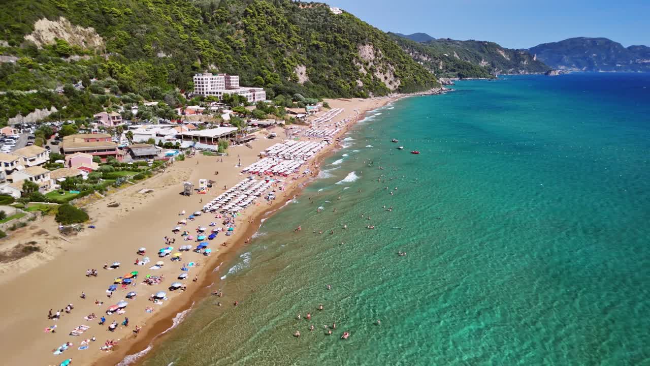 Sunny beach with clear waters and hills, people relaxing and playing