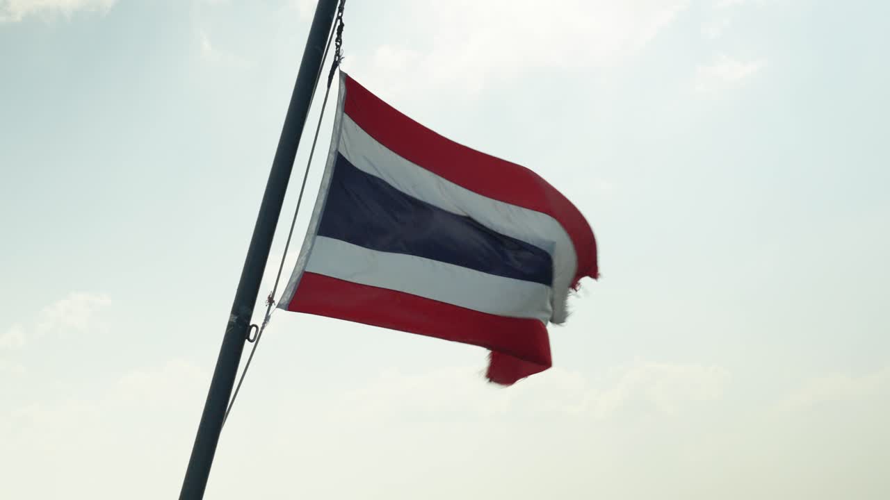 slowmotion of a Thai flag fluttering in the wind with a luminous sky behind, the flag is red, white and blue in horizontal lines.