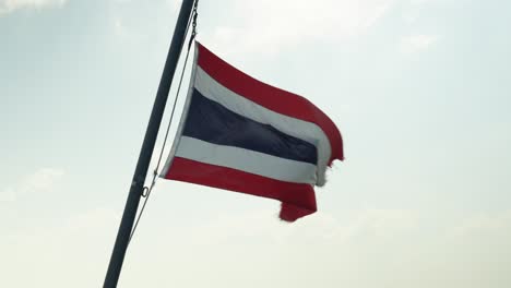 slowmotion of a thai flag fluttering in the wind with a luminous sky behind, the flag is red, white and blue in horizontal lines.