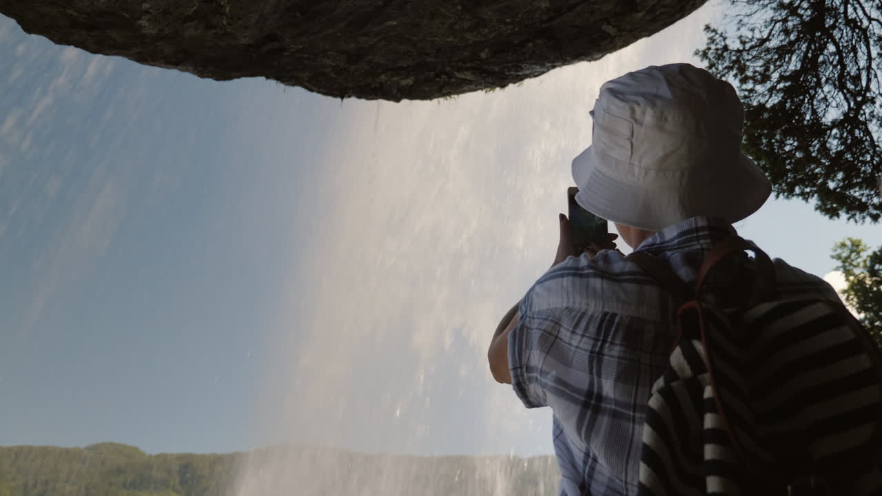 una mujer parada debajo de una cascada steinsdalsfossen toma una foto encima de ella cuelga una roca majestuosa