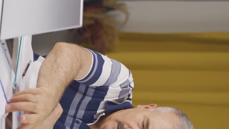 Vertical-video-of-Home-office-worker-old-man-gets-frustrated-while-looking-at-phone.