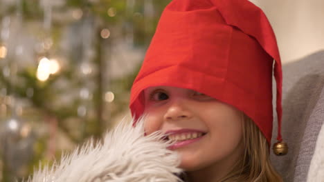 jovencita alegre con gorro de papá noel sonriendo alegremente con el fondo del árbol de navidad, de cerca