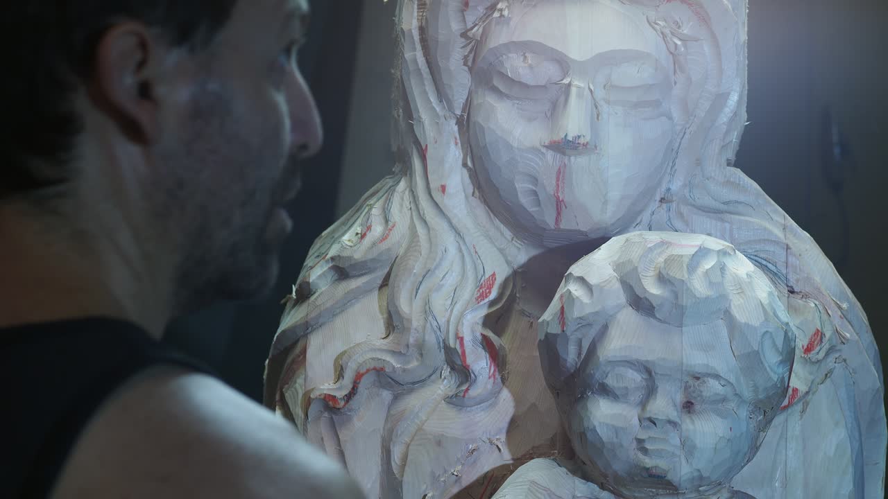 Skilled artisan attentively inspects partially carved wooden statue of the Madonna and Child, evaluating proportions and details during the delicate stages of religious sculpture creation, real time