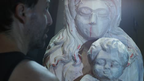 skilled artisan attentively inspects partially carved wooden statue of the madonna and child, evaluating proportions and details during the delicate stages of religious sculpture creation, real time