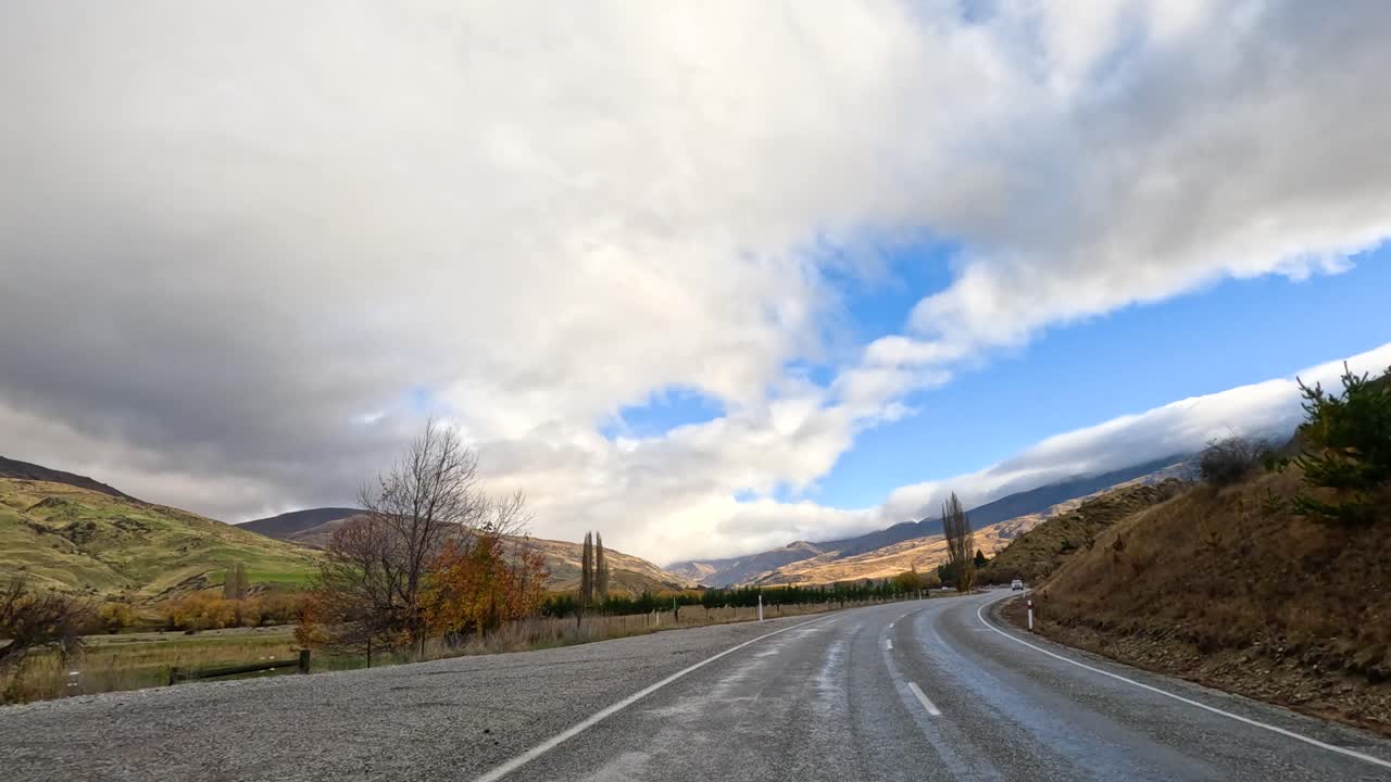 A serene drive along a winding road in Wanaka, New Zealand, showcasing autumn foliage under a dramatic sky