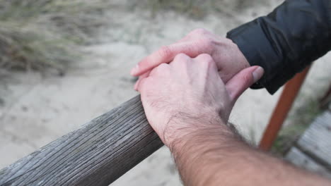 one male hand is resting on a wooden rail