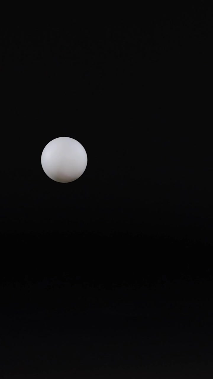 A white spherical ball travels horizontally across a dark, minimalist grid in a vertical frame.