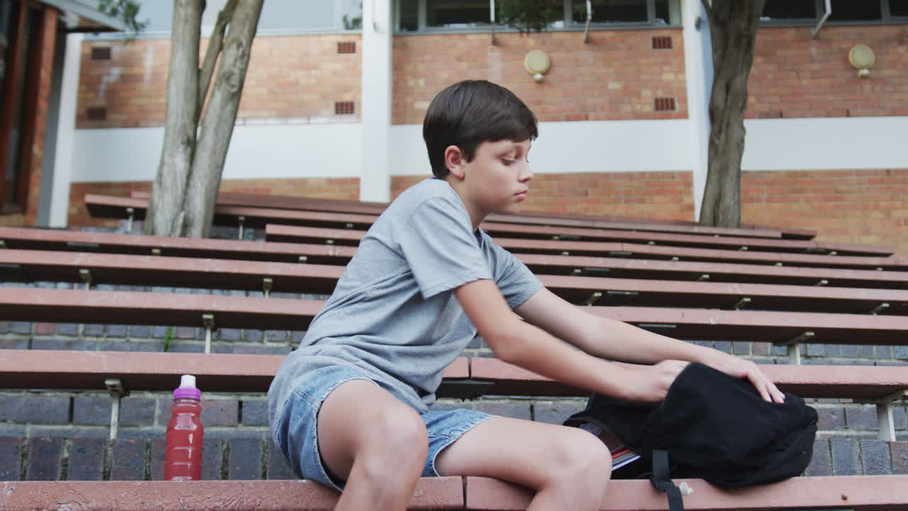 Sitting on school steps, boy holding apple and juice bottle, backpack beside him, copy space
