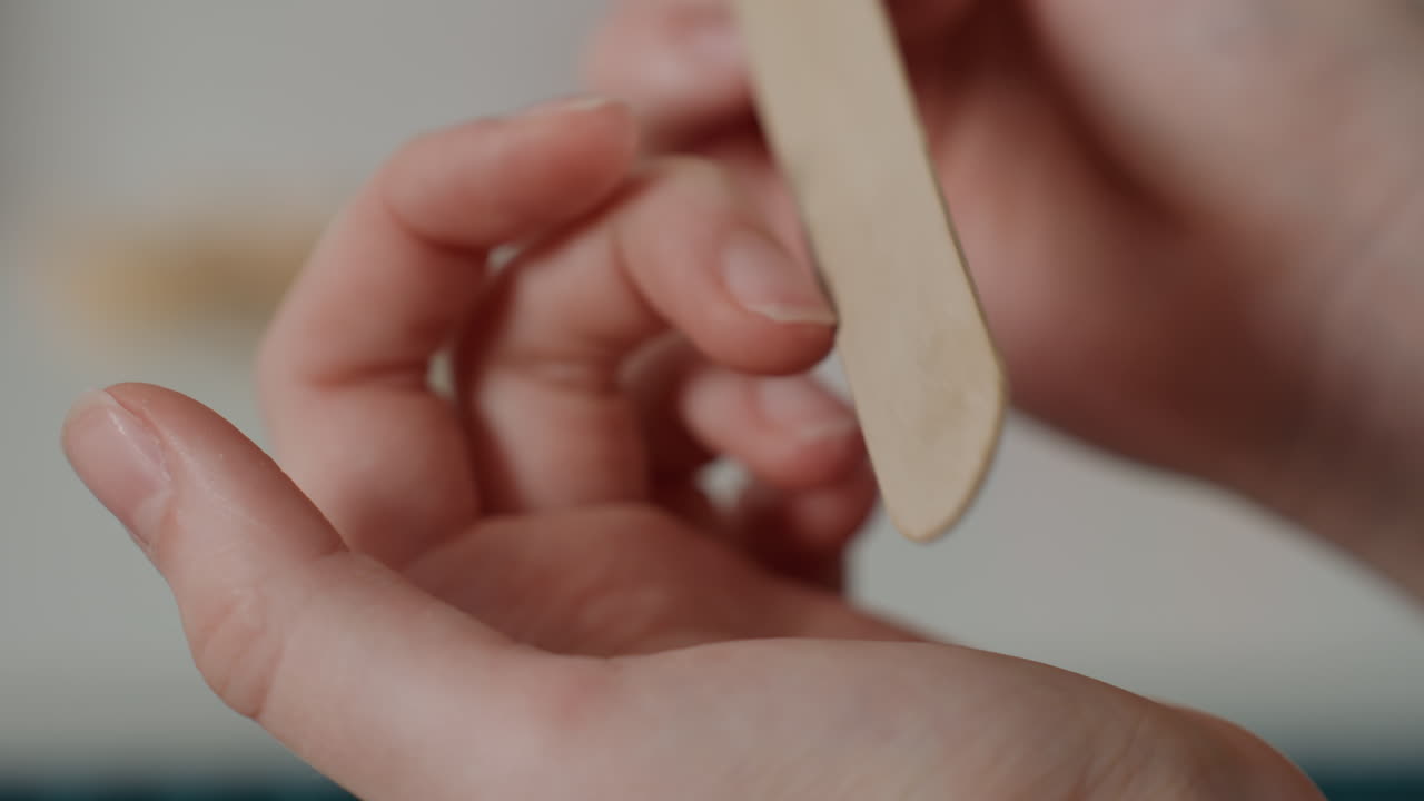 Primo piano di mani che preparano le unghie con una spatola, strumento di legno usato per spingere le cuticole, movimenti precisi, illuminazione da studio pulita, mani ferme del tecnico, preparazione accurata per finitura e smalto.