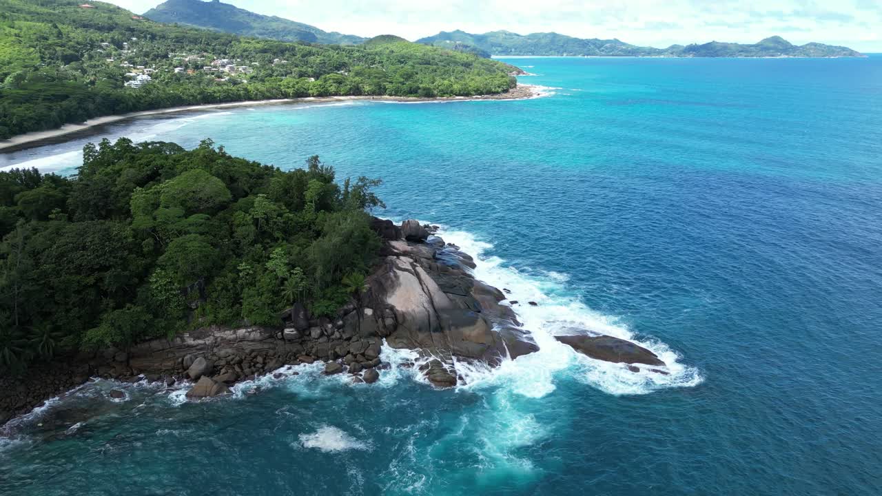 Mahe Island, Seychelles archipelago drone approach scenic coastline with waves crash in to cliff covered in green palm tree jungle vegetation
