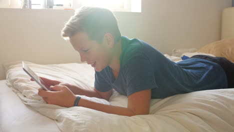 boy lying on bed using digital tablet