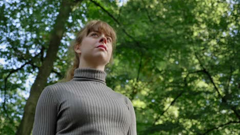 Beautiful-young-woman-looks-up-at-green-forest-canopy,-low-angle