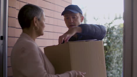 back view of short haired woman receiving cardboard box from courier and signing document at home