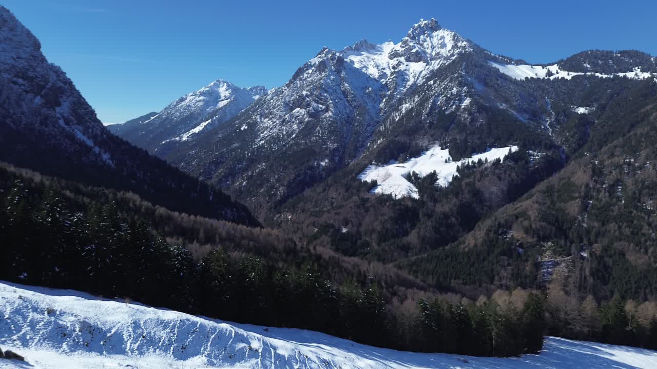 vista aérea de huellas en la nieve en un camino de montaña con bosque de pinos y montañas cubiertas de nieve en el fondo en un día soleado con un cielo azul claro en los alpes austriacos