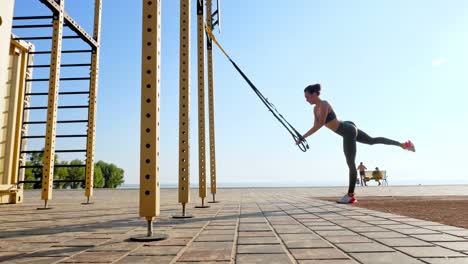 entrenamiento al aire libre. correas de suspensión. entrenamiento con correas. mujer joven atlética está haciendo ejercicios de resistencia de todo el cuerpo usando cuerdas en bucle trx, en la playa durante la puesta o el amanecer. entrenamiento de fitness al aire abierto. concepto de estilo de vida saludable. deporte matutino