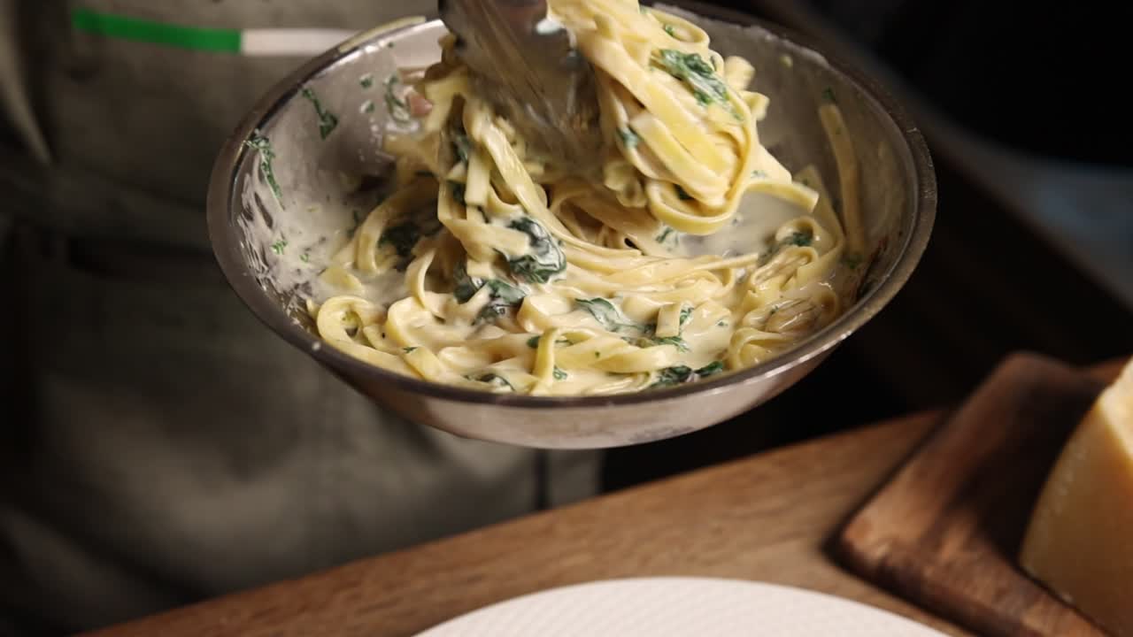 Chef che mescola fettuccine cremose con spinaci in una ciotola