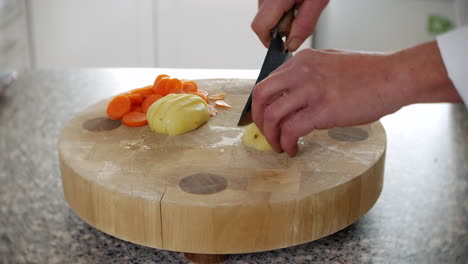 a chef is chopping a potato into wedges for chips and fries in a kitchen on a chopping board with a knife