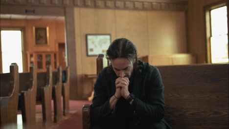 young man in black suit praying in an old church in cinematic slow motion