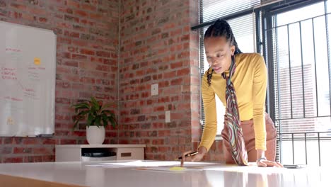 mujer de negocios afroamericana leyendo notas y documentos en una oficina soleada