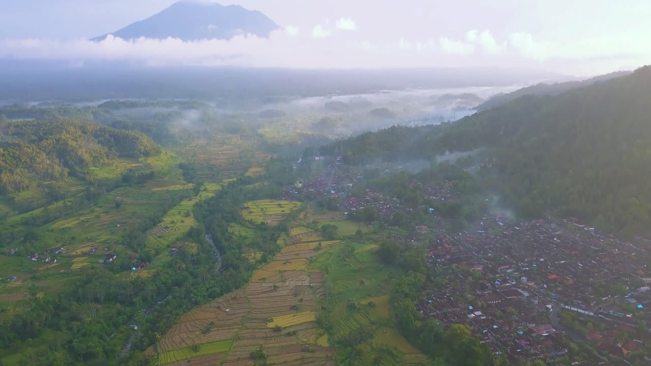 fotografía temprana de una ciudad al lado de terrazas de arroz y un volcán con nubes bajas
