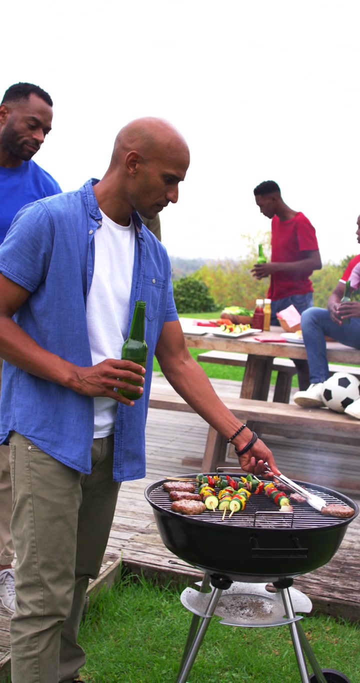 Diversi amici si riuniscono per un barbecue in terrazza, l'ospite gira spiedini e hamburger, con spazio per il testo