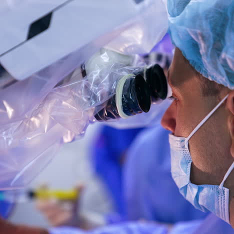 caucasian male doctor in mask and cap looks at microscope. side view close up portrait of a surgeon performing operation.