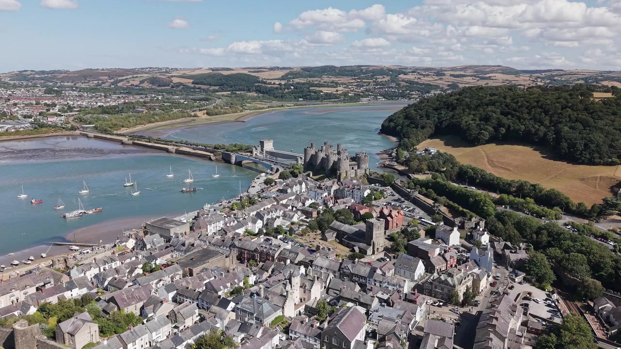 Drone flying forward over historic town rooftops toward medieval castle and estuary bridge on sunny day, an exceptionally preserved medieval fortification