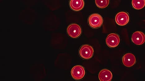 overhead shot of romantic lit red candles on background covered in rose petals with copy space