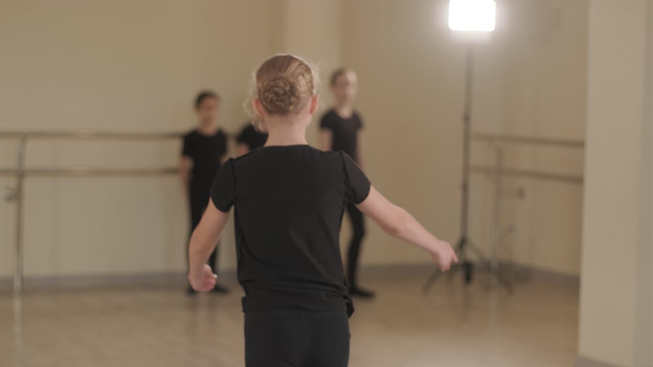 Un gruppo di giovani allievi di danza classica in abbigliamento da ballo nero che eseguono esercizi in un ampio studio di danza con pavimenti in legno e barre a muro. Espressioni concentrate e movimenti sincronizzati