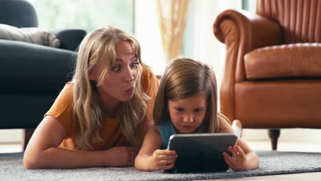 Familie-Mit-Mutter-Und-Tochter,-Die-Zu-Hause-Im-Wohnzimmer-Auf-Dem-Boden-Liegen-Und-Mit-Einem-Digitalen-Tablet-Spielen