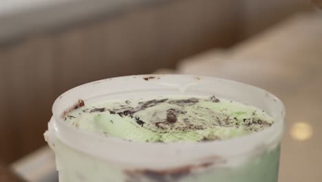 hands scooping green ice cream with chocolate from a container