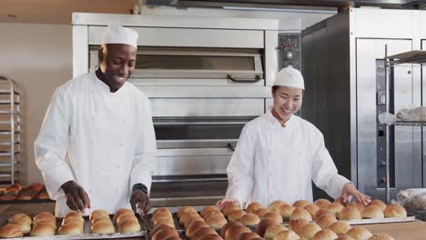 portrait of happy diverse bakers working in bakery kitchen with fresh rolls in slow motion